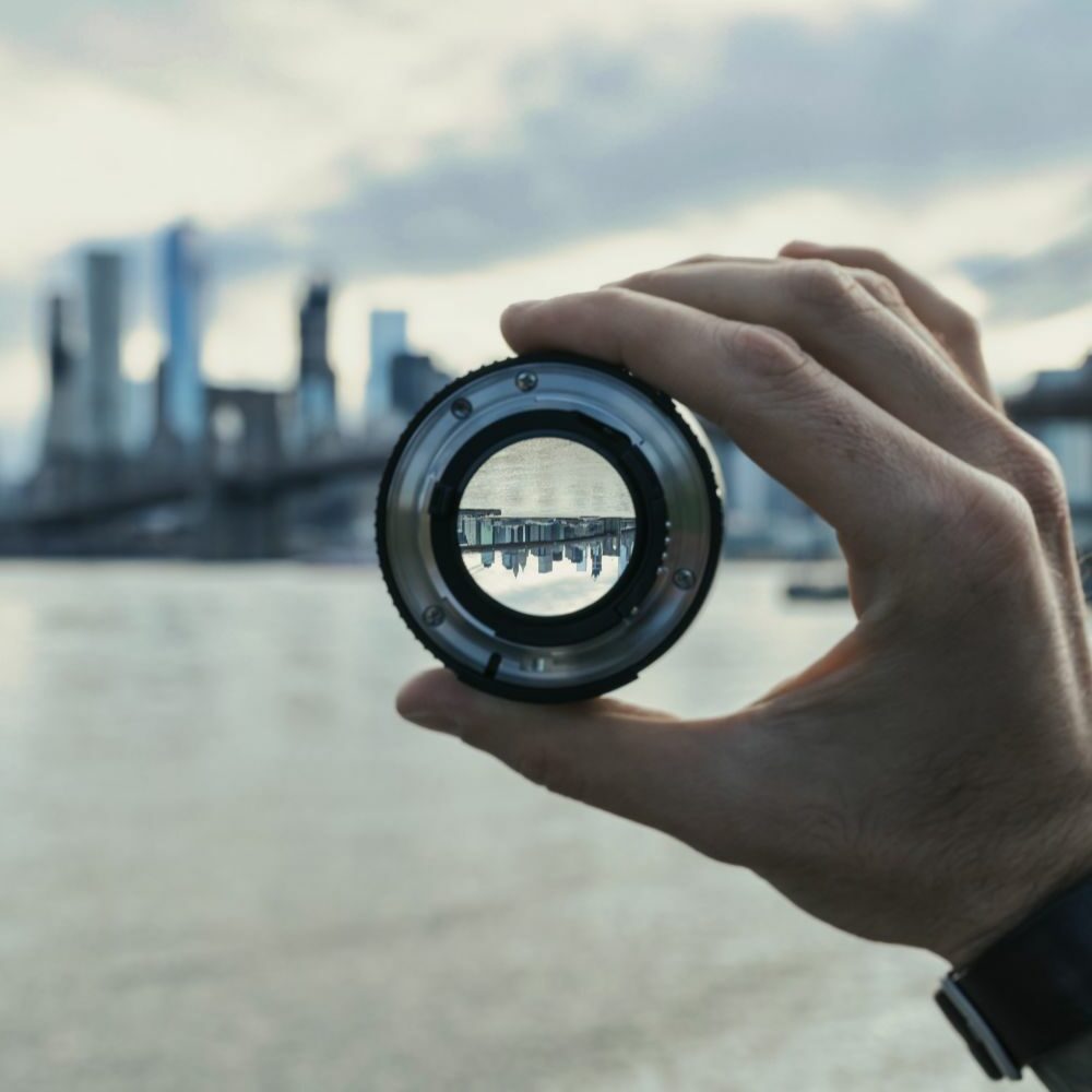 a hand holding a camera lens where you can see an upsidedown city